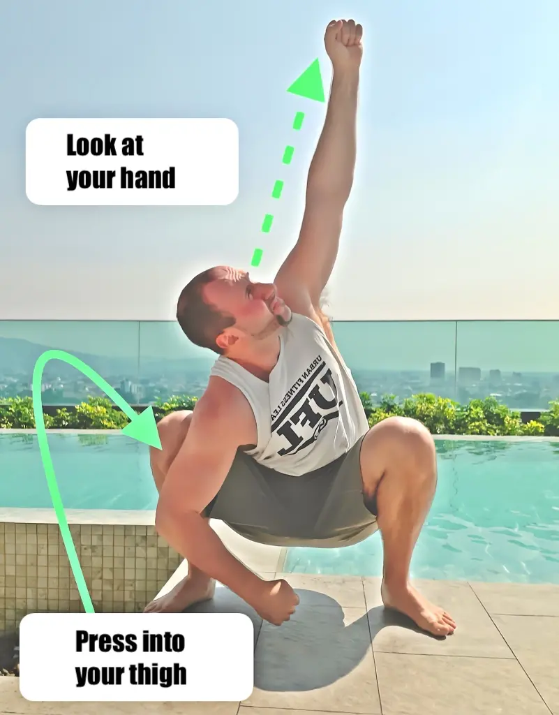Deep squat variation with the right arm pressing into the inner thigh and the left arm raised up towards the sky
